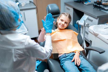 Friendly dentist giving high five little girl sitting on stomatological chair after treatmentの写真素材