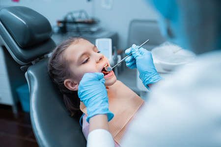 Side view of little girl who sits dentists chair where female dentist examine her teeth. Dentistryの写真素材