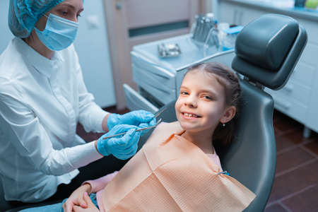 Cute young girl visiting dentist, having his teeth checked by female dentist in dental officeの写真素材