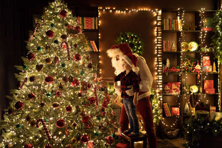 Santa Claus with little boy having fun by the fireplace while decorates Christmas tree