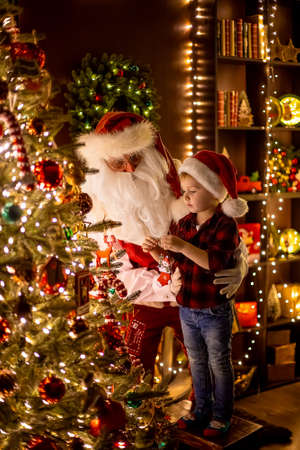 Santa Claus decorating Christmas tree with little boy assistant at home. New Year, Happy childhoodの写真素材