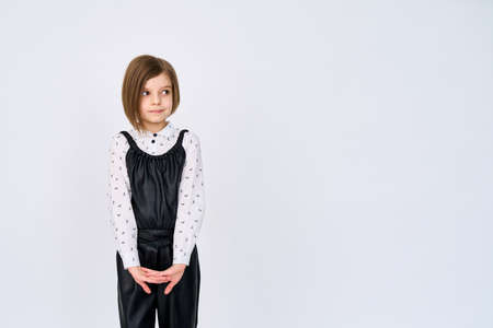 Little child girl in black white clothes stands over white background while looking sidewaysの写真素材