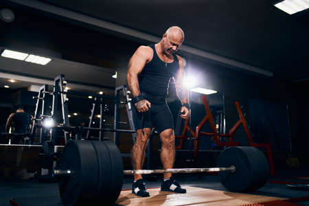 Older powerlifter preparing to exercise deadlift with barbell while on cross training in a gym.の写真素材