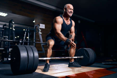 Older bodybuilder preparing to exercise deadlift with barbell while on cross training in a gym.の写真素材