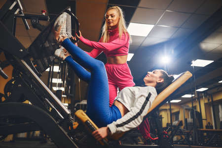 Personal trainer helping woman in works out on training apparatus inside in fitness center. Sporty lifestyle, bodybuilding, training conceptの写真素材