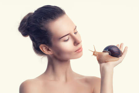 Beautiful adult girl holds giant Achatina snail on light background. Beauty treatments anti-agingの写真素材