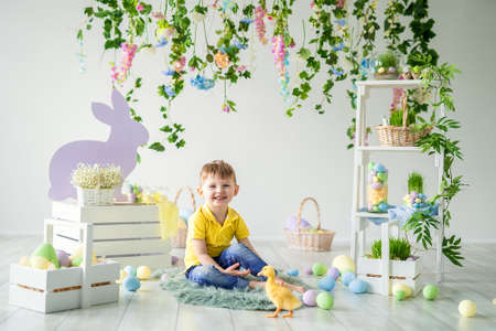 Happy little boy sits on wooden floor with little duckling in Easter decoration. Easter for children