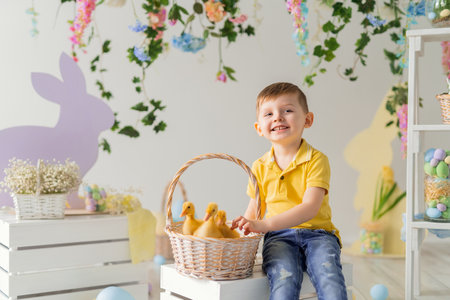 Happy child boy sits near the basket with fluffy ducklings on the wooden box. Easter decoration.