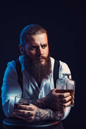 Dramatic portrait of bearded man who holds whiskey in his hands, dressed in white shirt. Studio shotの写真素材