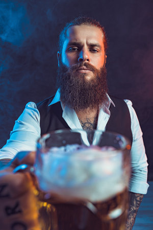 Serious bearded man holds out tasty draft beer to the camera. Drinking, October fest concept.