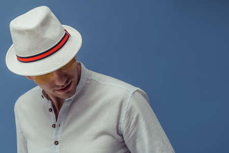 Studio portrait of young man who wears in sunglasses with elegant white hat on colorful background