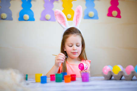 little girl in Easter bunny ears painting Easter eggs at home prepares to Easter. Happy easter