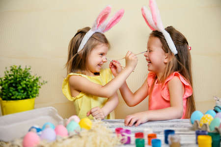 Two little girls in bunnies ears paint Easter eggs and pait each othes. Preparing for Easterの写真素材