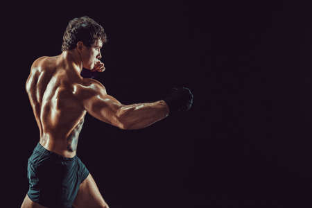 Side view of boxer in red gloves who practicing swing on black background. Sport conceptの写真素材