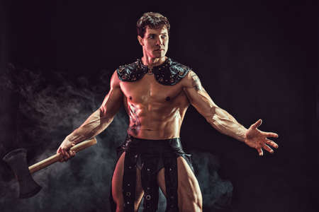 portrait of muscular gladiator who holds axe and looking away while posing in smoke background.の写真素材