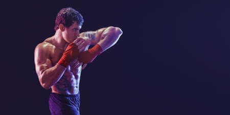 Side view of muscular kickboxer who delivering elbow hit isolated on black background. Mixed mediaの写真素材