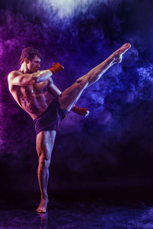 Full size of muay thai fighter who delivering leg kick to the head on smoke background. mixed mediaの写真素材