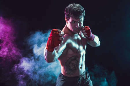 Studio shot of shirtless boxer fighter who preparing for fight on smoke background. Sport conceptの写真素材
