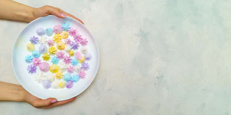 Top view of hands wich holds plate with delicious colorful meringue cookies. Sweet decor.の写真素材