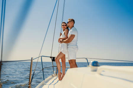 happy young couple in white clothing standing together on yacht while looking at the blue seaの写真素材