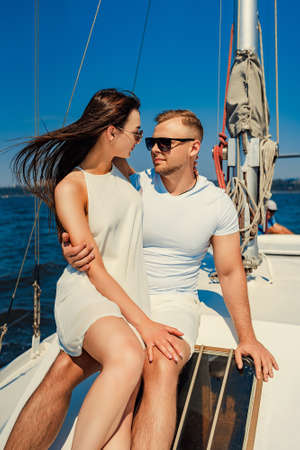 happy young couple in white clothing sitting together on yacht while looking to each other