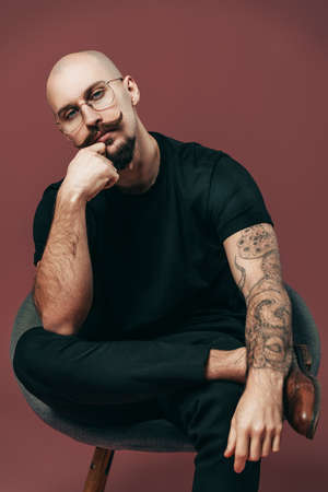 Thinking handsome bearded man in glasses with moustache sitting on chair on colorful background
