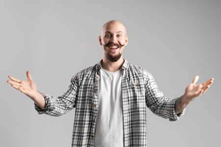 Portrait of bald bearded man in plaid shirt raising hands in gesture welcome on gray backgroundの写真素材