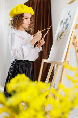 Little girl painting a picture in a studio or art school. Creative pensive painter child paints a colorful picture on canvas in workshop. Talented kidsの写真素材