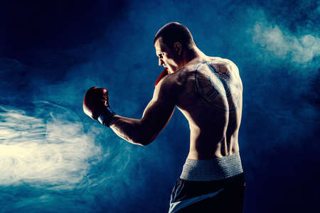 Side view of sportsman muscular boxer who fighting on black smoke background. Boxing sport conceptの写真素材