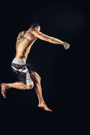 The professional athlete boxer in jump isolated on dsrk studio background. Fit muscular caucasian athlete fightingの写真素材
