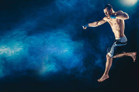 The professional athlete boxer in jump isolated on dsrk studio background. Fit muscular caucasian athlete fightingの写真素材