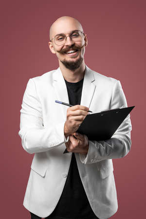 Balded man with mustache and beard in a business suit holding clipboard and pen isolated background.Concept of teacher, psychologist, student, lecturerの写真素材