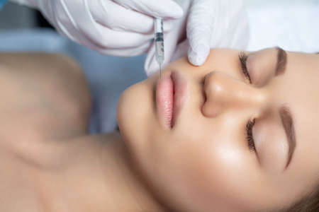 Attractive young woman is getting a rejuvenating facial injections. She is sitting calmly at clinic....