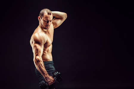 Powerful man doing the exercises with dumbbells. Photo of young man with good physique isolated on black background.の写真素材