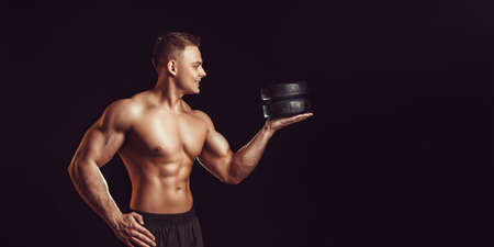 Power, strength, excellent body, bodybuilding, sports concept. Young handsome muscular fit man demonstrating perfect body and hold circles of cheese in black waxの写真素材