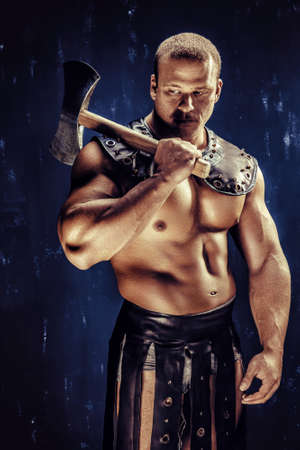 Studio shot of muscular ancient warrior man posing with axeの写真素材