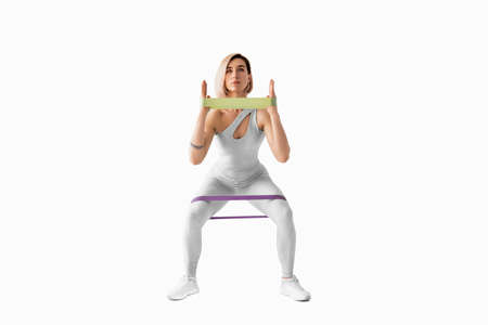 Sexy woman in sportswear using a resistance band in her exercise routine. Young woman performs...
