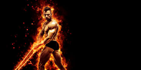 Body builder with fit torso belly chest and arms biceps triceps muscles holding chain while posing over the black background with fire. Bodybuilding conceptの写真素材