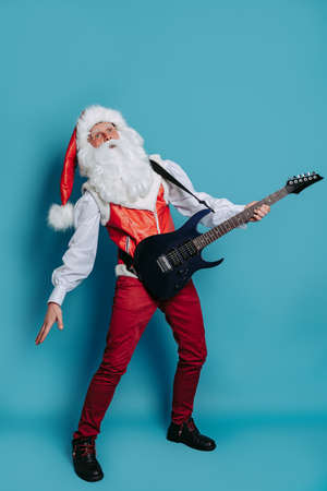 Full size of Cool Santa Claus who stands with electric guitar on blue background. Christmas party.の写真素材