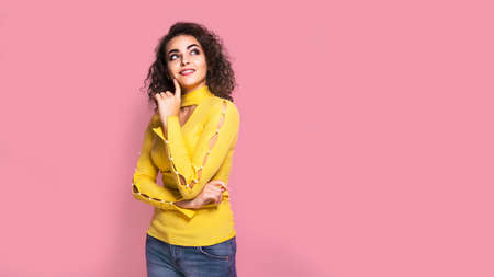Beautiful young curly caucasian girl in a yellow outfit , who is smiling and posing on pink backgroundの写真素材