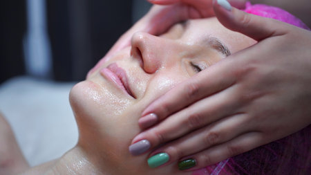 Attractive female at spa health club getting a facial massage. Beautician doing massage of face,...