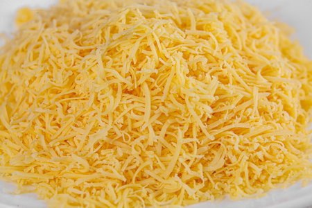 Closeup of grated cheese in white plate on white background. Topping. Cooking concept