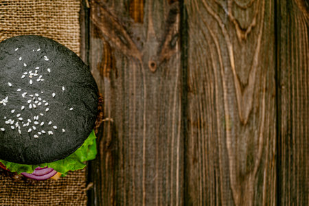 Top view of appetit black burger with meat cutlet and vegetables on rustic wooden table. Copy Spaceの写真素材