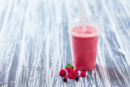 Front view of berries milkshake in plastic cup with ingredients on wooden background. Space for textの写真素材
