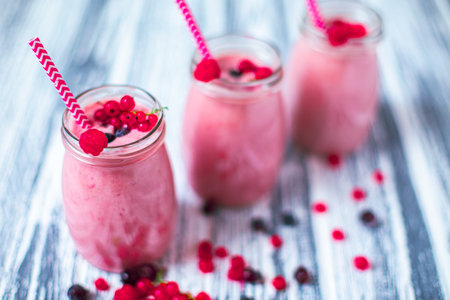 Front view of three berries milkshakes in glasses jars with ingredients on wooden backgroundの写真素材