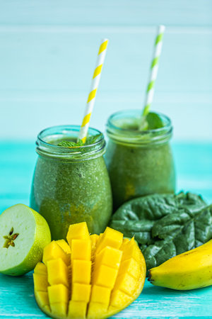Freshly blended green smoothie with mango, apple and banana in glass jars. Turquoise blue backgroundの写真素材