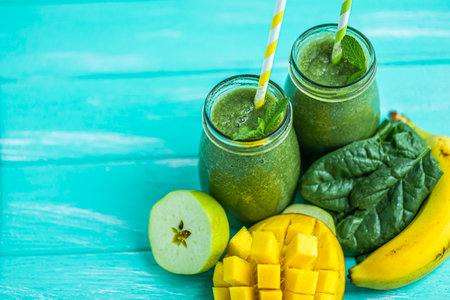 From above view of green smoothie with mango, apple, banana in glass jars. Turquoise blue backgroundの写真素材