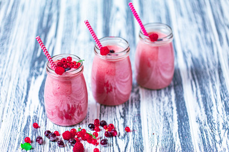 Front view of three berries milkshakes in glasses jars with ingredients on wooden tableの写真素材