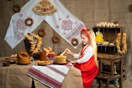 Little girl in folk Russian costume sprinklers pancakes with honey while celebrating Maslenitsaの写真素材