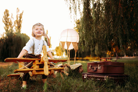 Happy little pilot boy in vintage aviation hat looking forward outdoor sitting on wooden planeの写真素材